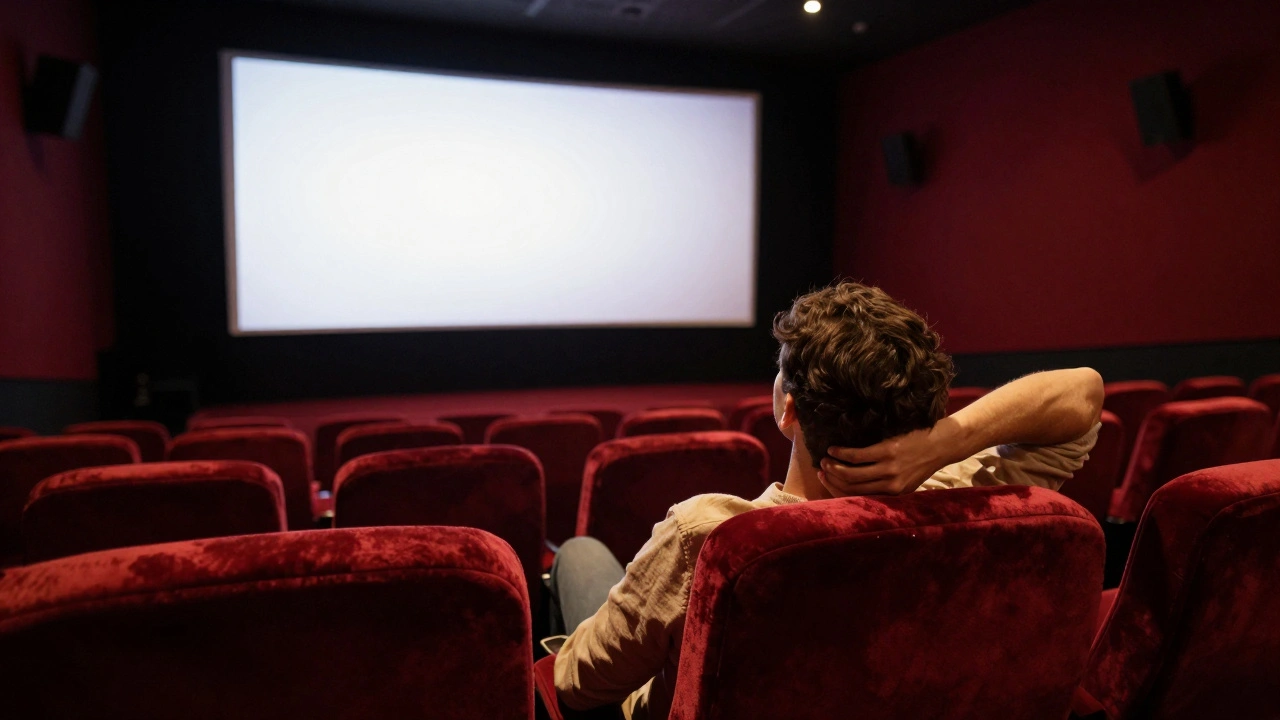 Person relaxing in a red velvet cinema seat, watching a glowing screen in a dark theater.