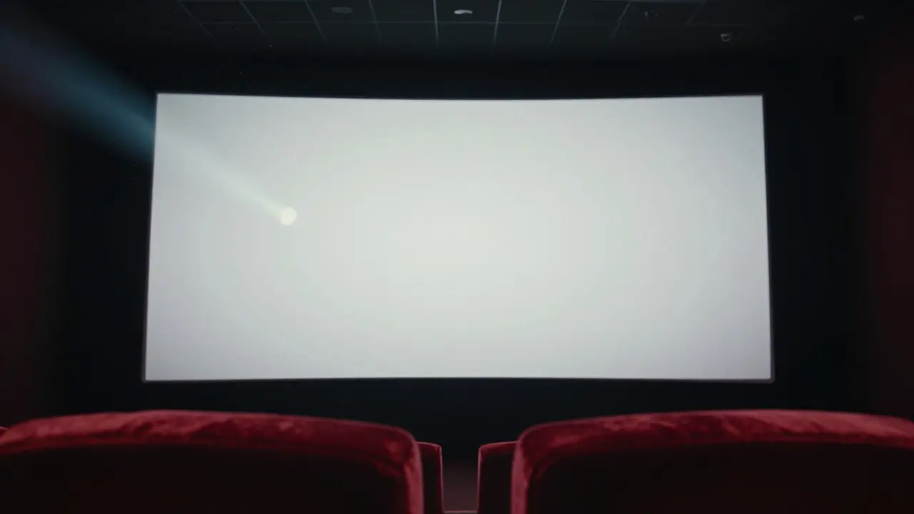 Empty seats in a dark movie theater facing a blank white screen with projector light