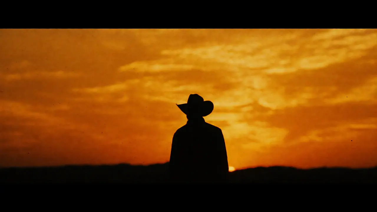 Silhouette of a cowboy against a bright sunset sky with strong backlighting.